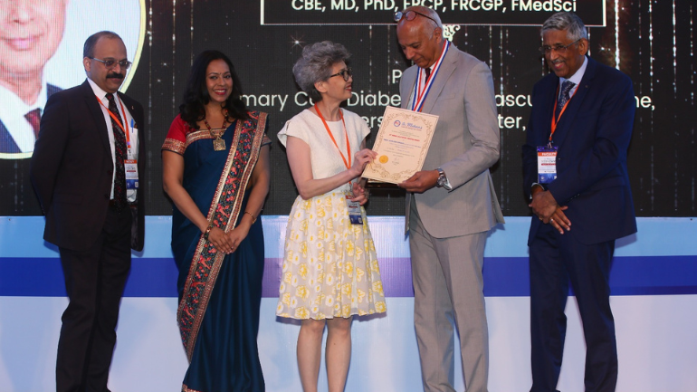 Kamlesh Khunti on a stage receiving his award as people look on and clap.