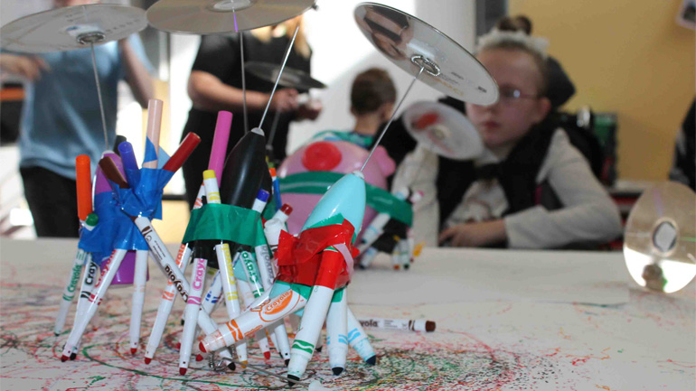 Child looks at a sculpture made from felt pens and CDs