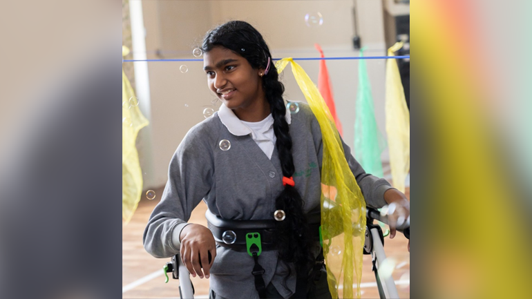 Young girl with walking aid smiles surrounded by bubbles and fabric