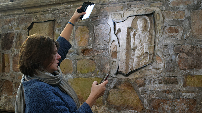 Professor Joanna Story holds a light to a wall engraving at Breedon on the Hill, Leicestershire