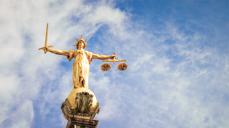 A telephoto image of the statue of Lady Justice, holding a sword and weighing scales, located on top of the Central Criminal Court, known as the Old Bailey, in London.