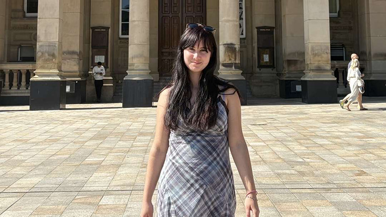 Rosie standing in front of a historic building with stone columns on a sunny day.