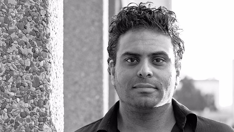 Portrait of Haresh Sood standing beside a textured wall.