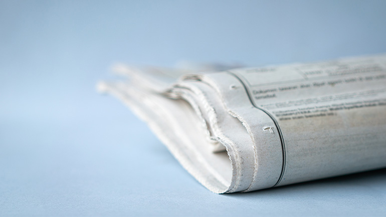 Folded newspaper on a light blue surface, representing local journalism and news reporting.