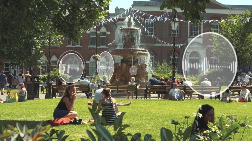 A group of people sat in front of Leicester Town Hall with digital icons representing noise pollution.
