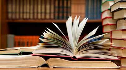 Stack of books on a table with one laying open.