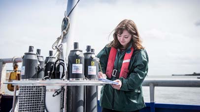 Female scientist making notes with sea water sampling experiment on research ship.