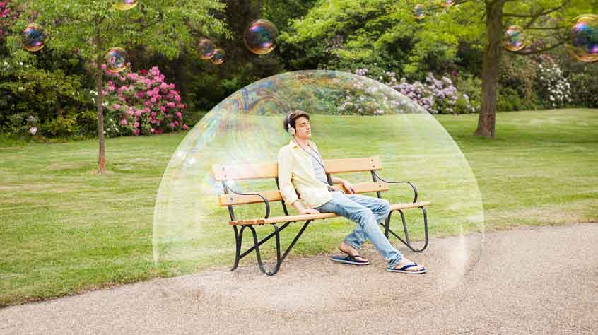 Man sitting on a bench with a big bubble around him.