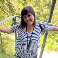 Photograph of Patricia. Patricia is standing on a balcony surrounded by trees, and is smiling