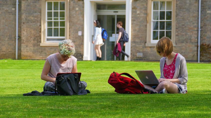 Two students sat on the lawn outside the Fielding Johnson building working on laptops.