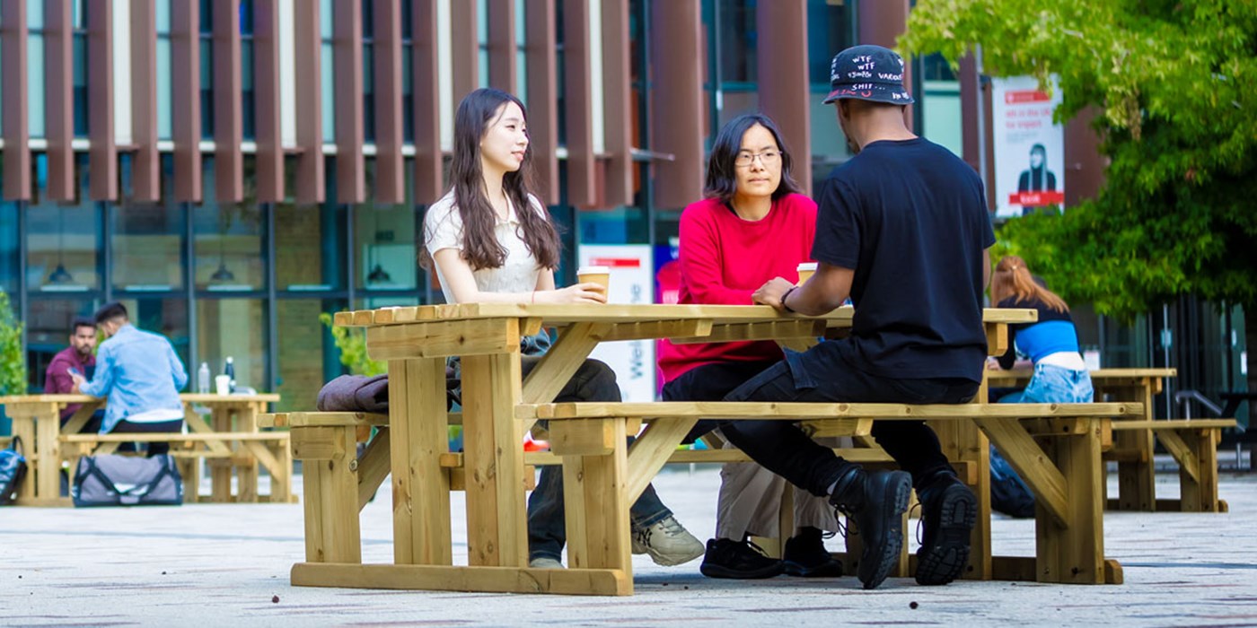 Students sitting on benches in Centenary Square, with the Percy Gee building in the background