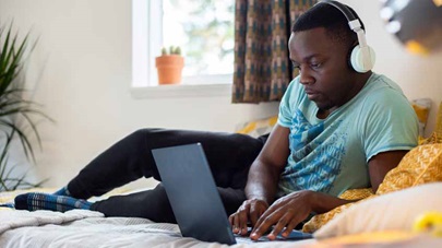 Student on bed in halls of residence working on a laptop