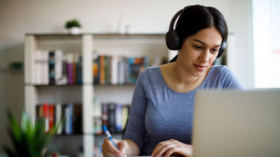 Woman working on a laptop wearing headphones.