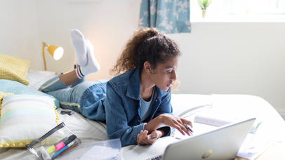 Student lying on her bed working on her laptop 