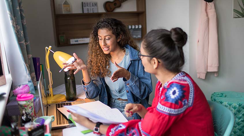 Two students chatting and studying sat at a desk