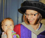 Lyndsay Poore at her PhD graduation, holding her daughter.
