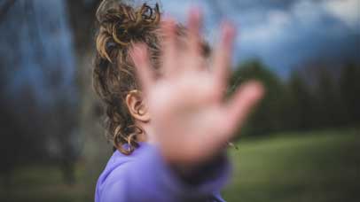 Little girl with curly hair holds hear hand out with fingers spread to block her face and to say stop with her hand.