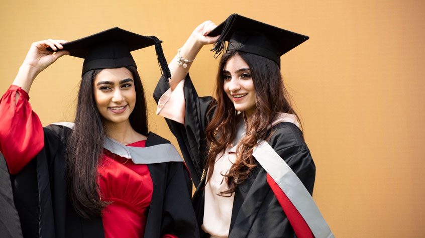Two students at graduation posing in their caps and gowns.
