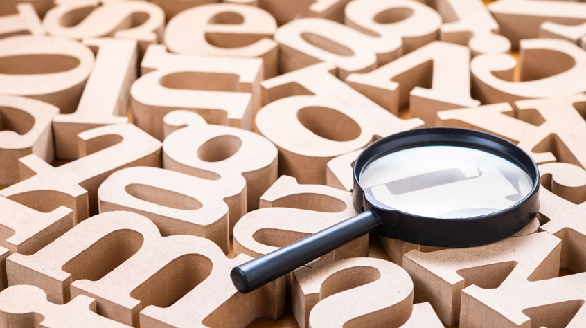 Wooden models of letters of the alphabet laying next to each other with a magnifying glass sitting on top of them.