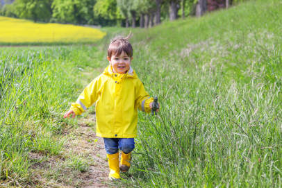Happy toddler running in field with yellow muddy welly's and yellow raincoat