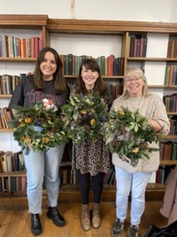 Three ladies holding their wreaths in front of the bookcase in Beaumont hall
