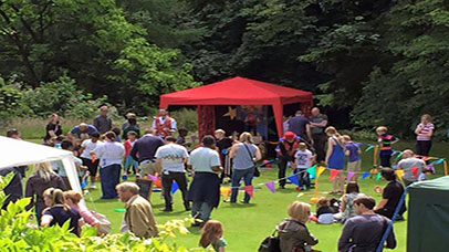 People gathered around a small tent in a garden in the sun.