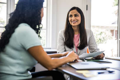 two females in formal interview setting speaking and smiling