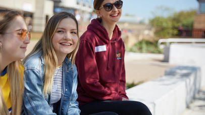Students sitting on a bench smiling at the camera on a sunny day
