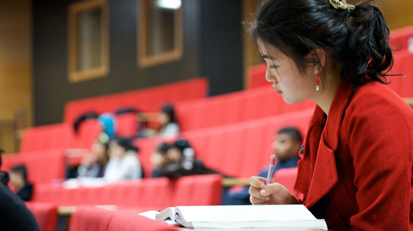 A student in a lecture theatre reading a textbook