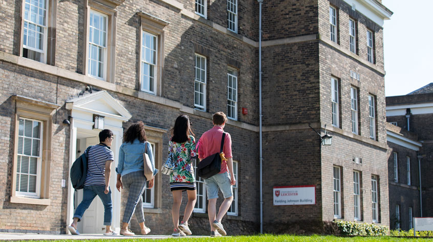 Four students walking past the Fielding Johnson building on University of Leicester campus.