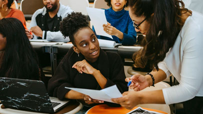 A teacher talking to a student at her desk.