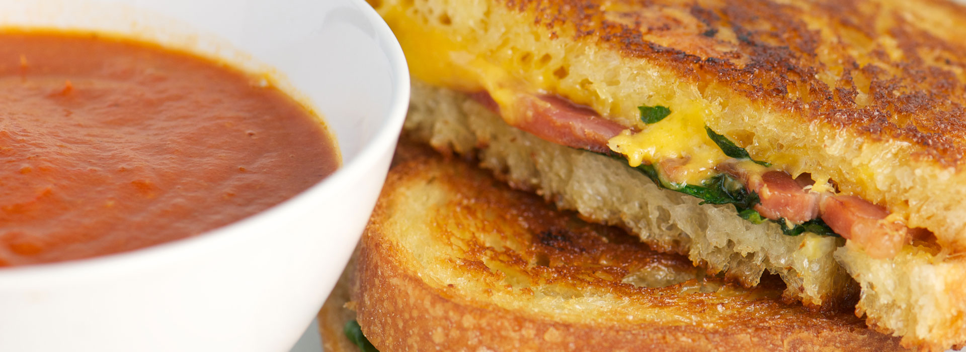 Grilled bacon, cheese and spinach sandwich with white bowl of tomato soup