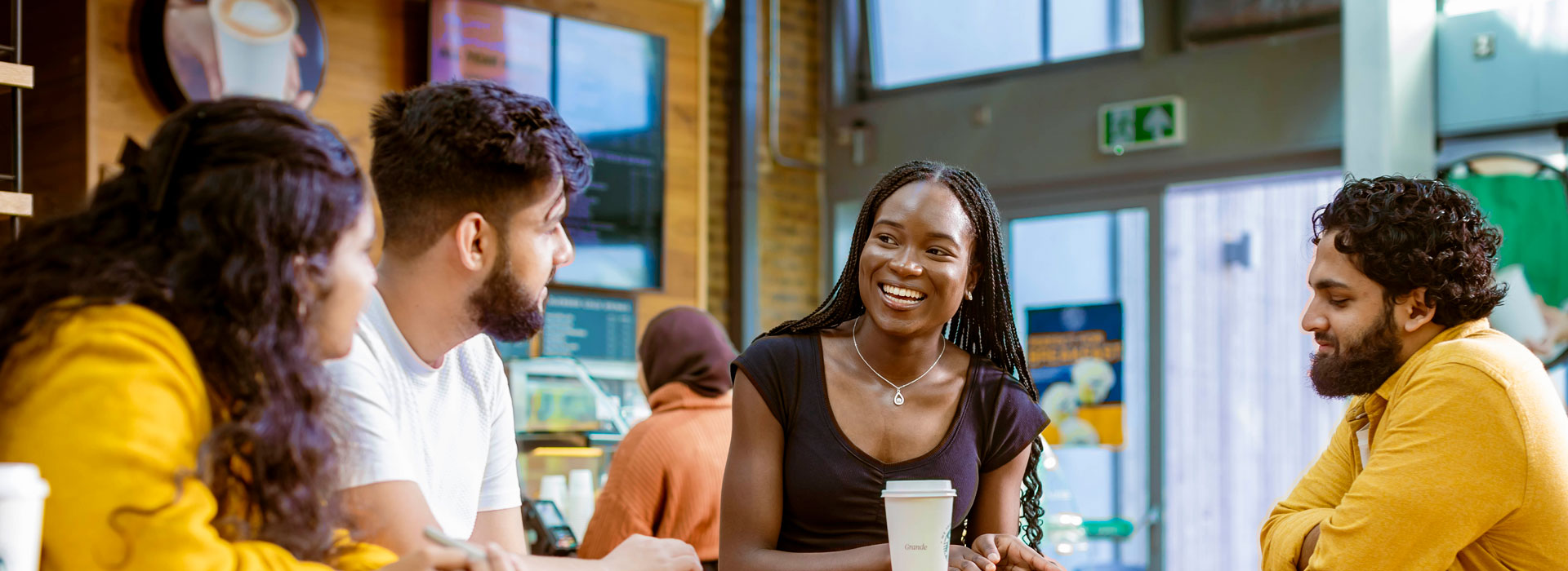 Four students sitting at a table in a university common area, talking and smiling.