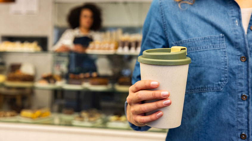 Person holding reusable coffee cup in a cafe
