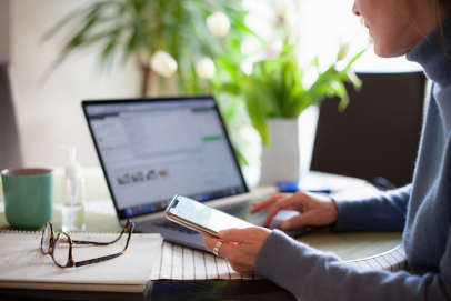 woman on laptop holding her iphone