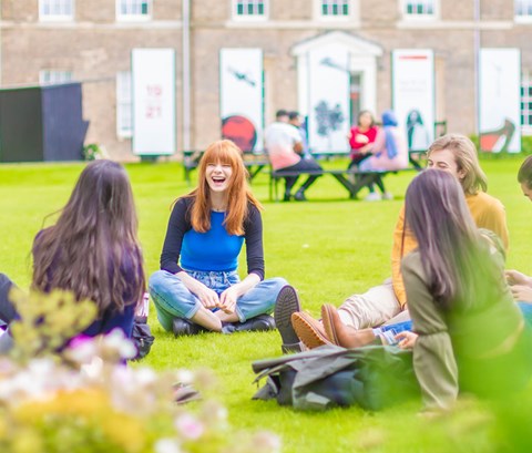 Students sitting on the grass in a circle outside the Fielding Johnson building on Leicester campus.