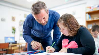 Teenager with down syndrome writing, with her teacher looking at her work