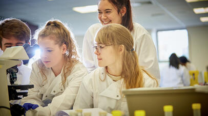 Group of people in lab coats next to microscope