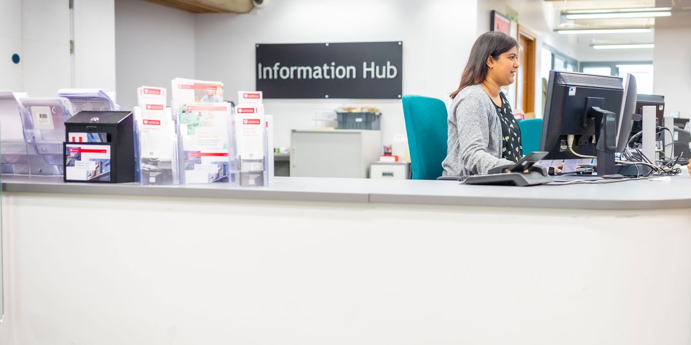 A student sitting at the information hub desk at the David Wilson Library on Leicester campus.
