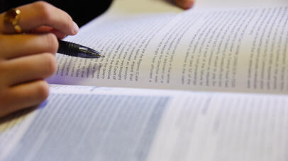Close-up image of someone reading a book with a pen in their hand. 