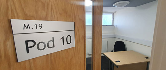 Photograph of an study room with one table and chair, with a sign on the door named "Pod 10"