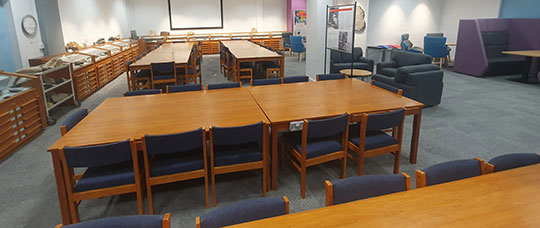 Photograph of multiple long tables for study with soft chairs and sofas in the background.