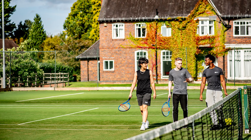 Three students walking towards a tennis pitch