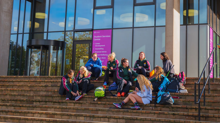 A sports team from the University sitting on the steps of the Charles Wilson building on campus.
