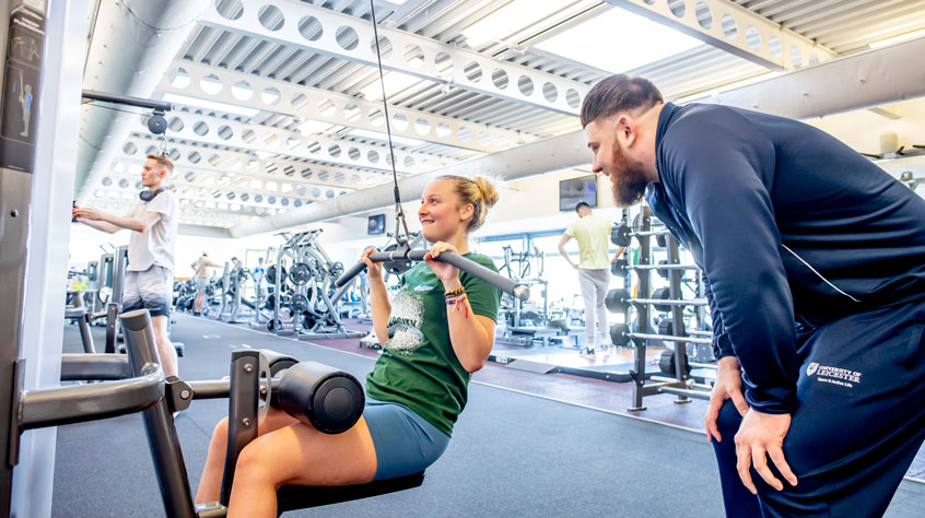 Coach working with a student on a weight-lifting machines