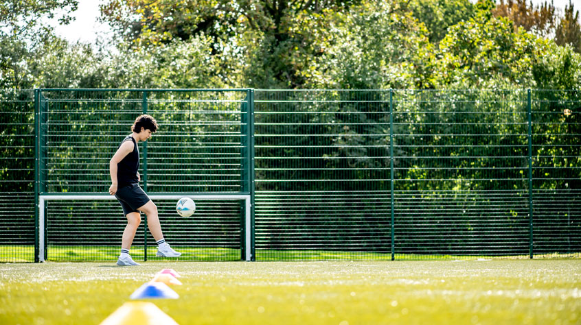 Student playing 'keepy uppys' with a football on a pitch