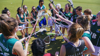 Team Leicester on a field in a big huddle putting lacrosse sticks into the middle of the huddle.