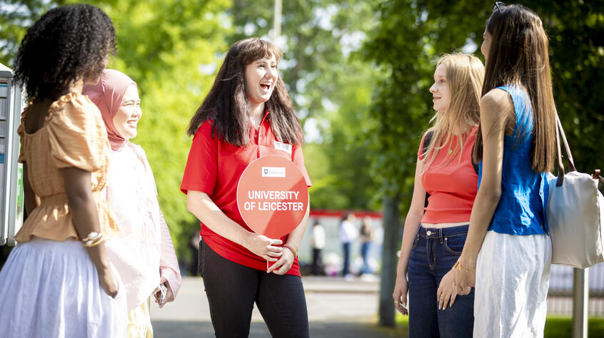 A group of young people standing around a tour guide on campus.