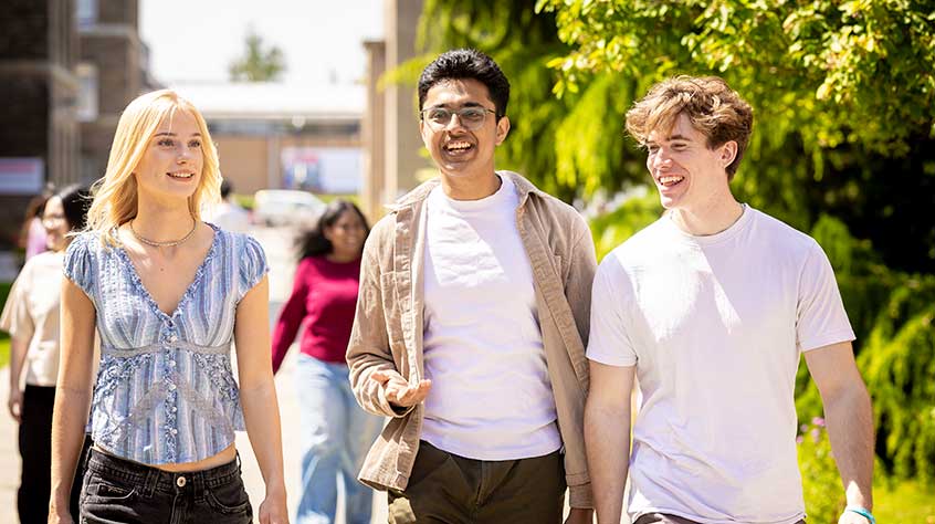 Photo of three students, one female, two male, walking through the centre of University of Leicester campus