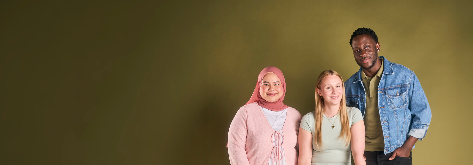 Three students, positioned to the right, smiling facing camera, solid gold colour background.